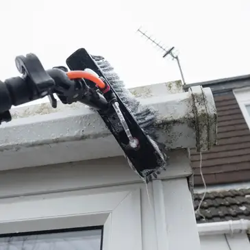 Gutter cleaning pole clearing moss from a house gutter