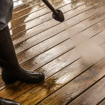 Decking being powerwashed, the cleaned boards a clearly lighter colour